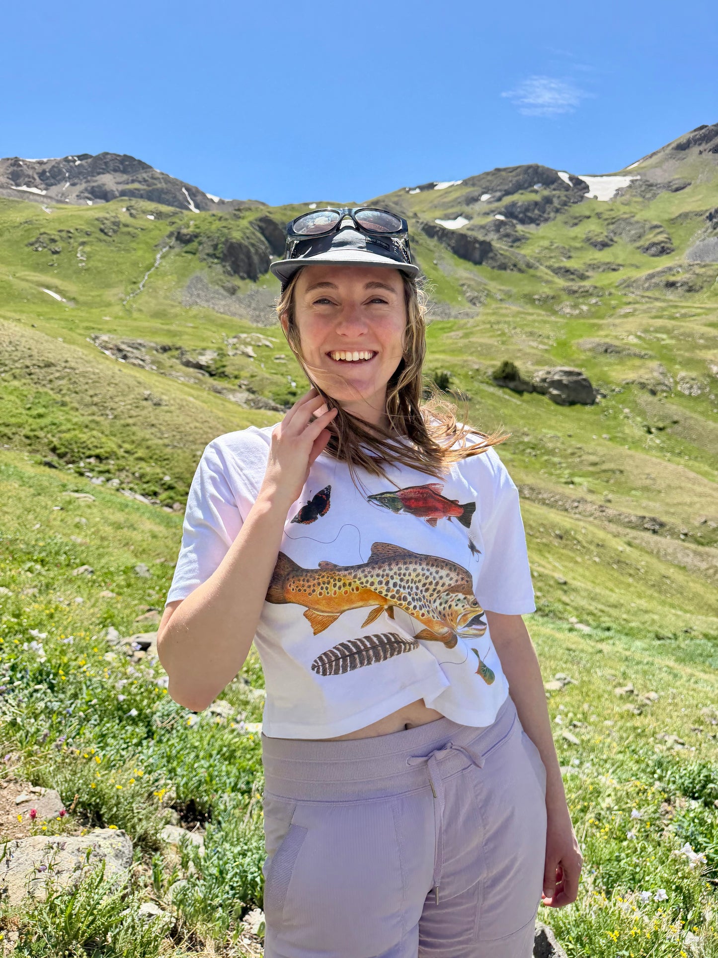 Person standing in a mountainous landscape wearing a t-shirt with fish design.